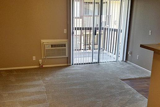 Carpeted living room, tan wall, built-in wall AC, balcony