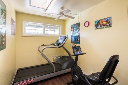 fitness center with two machines, ceiling fan, small window, posters on wall
