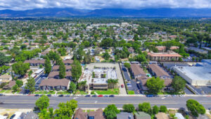 Aerial Exterior of Woodside Senior, Residential buildings, communities in the distance, mountains in the background, lush foliage, photo taken on sunny day with clouds.