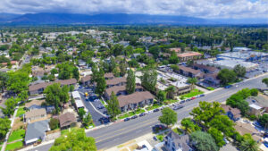 Aerial Exterior of Woodside Senior, Residential buildings, communities in the distance, mountains in the background, lush foliage, photo taken on sunny day with clouds.