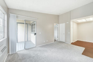 Interior Living room, Neutral gray carpeting, attached kitchen, wood floors in kitchen, sliding glass door to balcony, neutral toned walls.