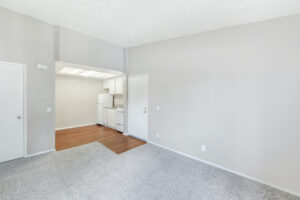 Interior Living Room, neutral gray carpeting, attached kitchen, wood floor in kitchen area, white appliances in kitchen, neutral toned walls.