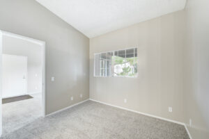 Interior Unit Bedroom, neutral toned walls and carpeting, window with view on balcony, high ceilings.