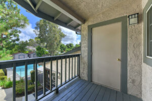 Exterior Unit Balcony, door to storage room, view of pool and lush foliage, photo taken on a sunny day.