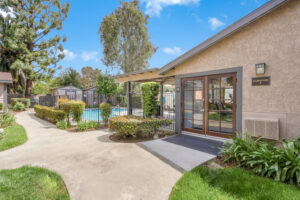 Exterior Woodside Clubhouse and pool area, pool area fenced in, meticulous landscaping, photo taken on a sunny day.